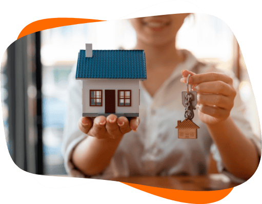 Mulher segurando e mostrando uma chave e uma casa miniatura nas mãos