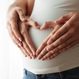 Homem e mulher segurando a barriga da mulher gravida.